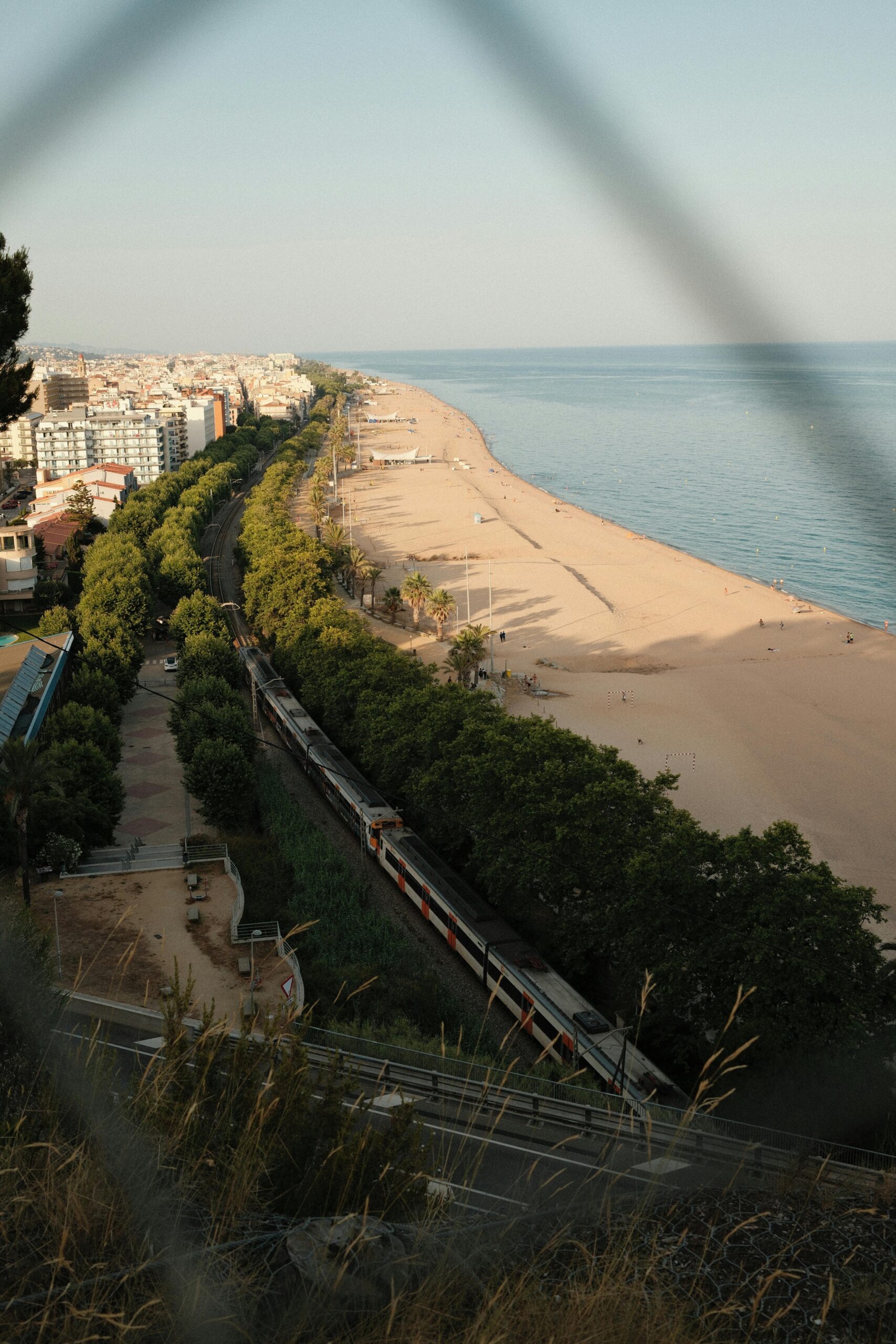 A scenic view overlooking a train alongside the beach and a coastal city at daytime.
